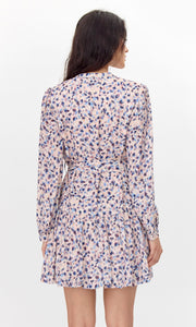 Model has back faced wearing a flowy long-sleeve dress with a pink, blue, and purple abstract print.