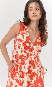 Close-u view of model placing her hands in both pockets of red and cream floral dress. The dress features a V-neckline and tie details on the side of the bodice.